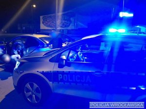 Radiowóz policyjny i policjanci zatrzymujący kierowcę samochodu osobowego