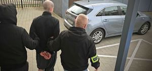 Zdjęcie przedstawia policjantów wydziału kryminalnego, którzy prowadzą zatrzymanego. Widok z tyłu