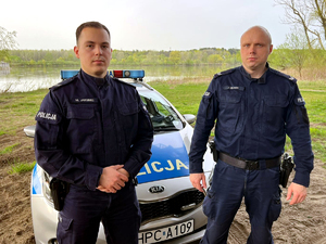 dwóch umundurowanych policjantów stoi na tle radiowozu