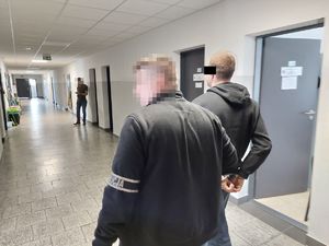 ubrany po cywilnemu policjant prowadzi korytarzem zatrzymanego