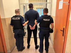 dwóch umundurowanych policjantów prowadzi zatrzymanego mężczyznę