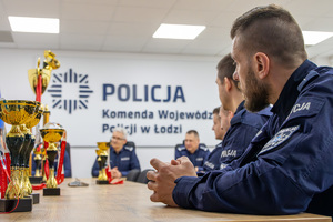 Komendant Wojewódzki Policji w Łodzi siedzi przy stole wraz z Zastępcami. Przed nim puchary.