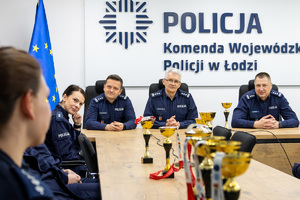 Komendant Wojewódzki Policji w Łodzi siedzi przy stole wraz z Zastępcami. Przed nim puchary.