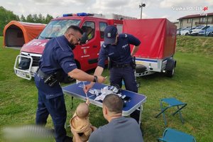Na zdjęciu widać policjantów przy stoisku promocyjnym, w tle pojazdy strażackie