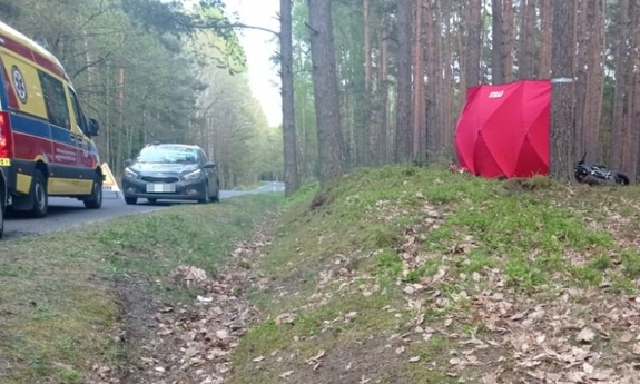 wypadek motocykla - karetka i samochód osobowy na poboczu drogi i zasłonięty po wypadku motocykl leżący koło drzewa