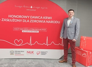 Na zdjęciu Łukasz Kaczyński stojący na tle planszy honorowy dawca krwi