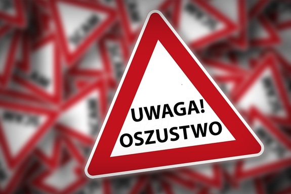 Na pierwszym planie wyraźny trójkątny znak ostrzegawczy z napisem Uwaga! Oszustwo. W tle widać pełno takich rozmazanych znaków