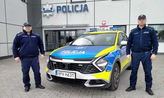 dwóch policjantów stoi koło radiowozu