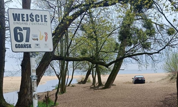 Tablica informująca o wejściu na plażę, w głębi widoczny pojazd, którego kierujący został ukarany