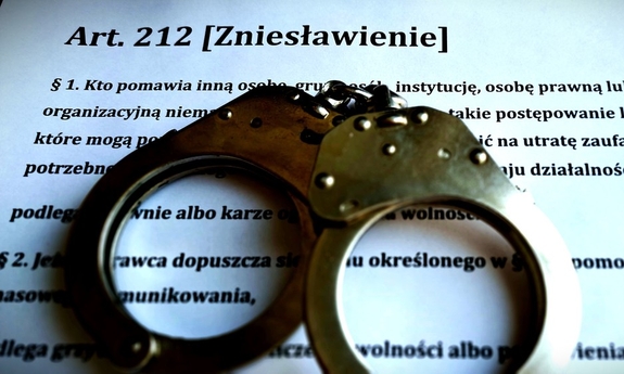 kajdanki leżą na kartce, na której jest wydrukowana definicja zniesławienia