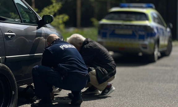 policjant wymienia koło w samochodzie seniora, on obok, a w tle radiowóz