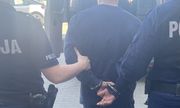 dwaj umundurowani policjanci prowadzą zatrzymanego, który na rękach trzymanych z tyłu ma założone kajdanki