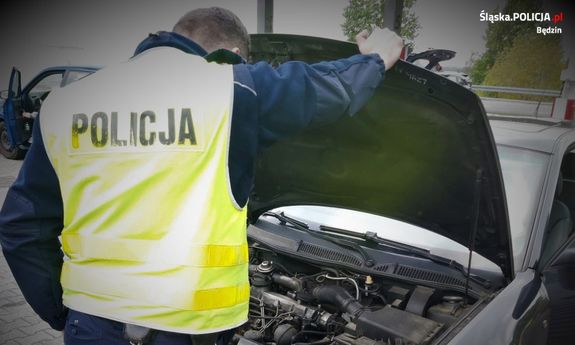 policjant w żółtej kamizelce z napisem Policja na plecach, zagląda pod maskę samochodu