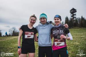 3 zawodniczki pozują do zdjęcia. w tle górka i las