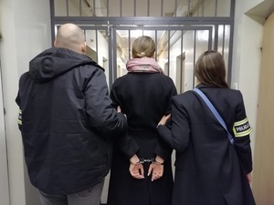 Policjant i policjantka prowadzą zatrzymaną korytarzem