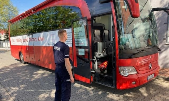 na zdjęciu umundurowany policjant stoi przed krwiobusem