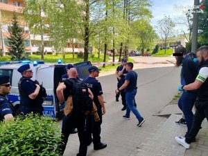 Zdjęcie przedstawiające policjantów, radiowóz oraz osobę zatrzymaną prowadzoną przez funkcjonariuszy