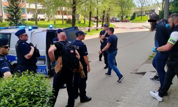 Zdjęcie przedstawiające policjantów, radiowóz oraz osobę zatrzymaną prowadzoną przez funkcjonariuszy
