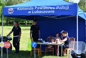 dwóch policjantów i policjantka w umundurowaniu służbowym, przebywający wraz z uczestnikami w niebieskim namiocie z napisem Komenda Powiatowa Policji w Lubaczowie