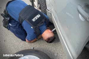 na zdjęciu umundurowany policjant w trakcie zmiany koła w samochodzie