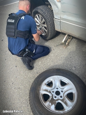 na zdjęciu umundurowany policjant w trakcie zmiany koła w samochodzie