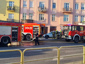 wozy strażackie przy budynku oraz strażacy i policjant