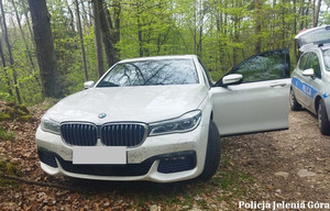 Jasne bmw stojące w lesie z otwartymi drzwiami od strony kierowcy obok radiowóz