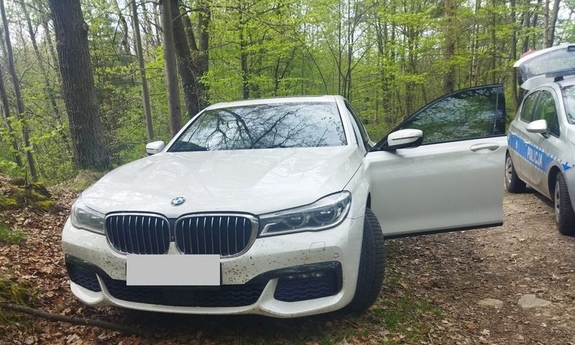 Jasne bmw stojące w lesie z otwartymi drzwiami od strony kierowcy obok radiowóz