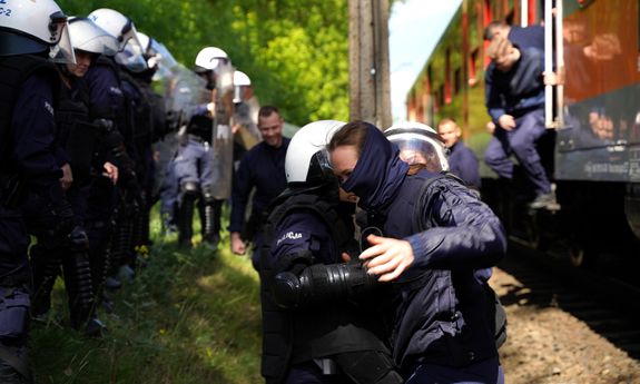 policjant trzyma uczestniczkę szkolenia, w tle pociąg i reszta policjantów