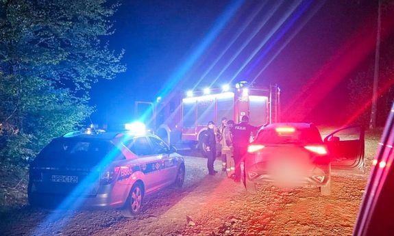 Radiowóz z włączoną sygnalizacją świetlną nocną porą, obok straż pożarna i samochód osobowy