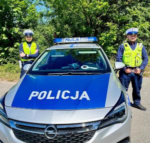 na zdjęciu policjantka i policjant stoją przy radiowozie