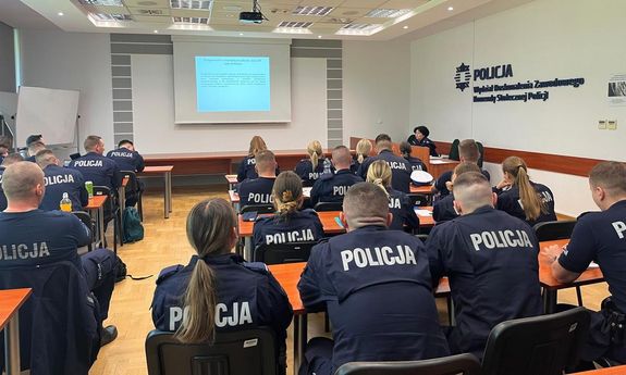 policjanci siedzą przy ławkach tyłem do aparat. patrzą na prezentację