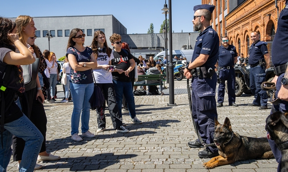 Przewodnik psa służbowego rozmawia z uczniami, obok niego na ziemi leży pies