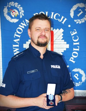 mł. asp. Łukasz Langa trzyma w dłoniach odznakę „Honorowy Dawca Krwi – Zasłużony dla Zdrowia Narodu&quot;
