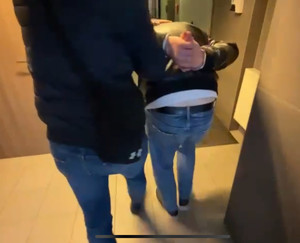 ubrany po cywilnemu policjant prowadzi zatrzymanego zakutego w kajdanki - widok z tyłu