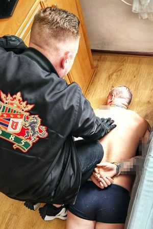 zatrzymany mężczyzna leży na podłodze zakuty w kajdanki obok niego kuca funkcjonariusz