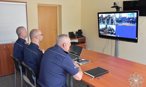 trzej policjanci siedzą naprzeciwko ekranu urządzenia do telekonferencji