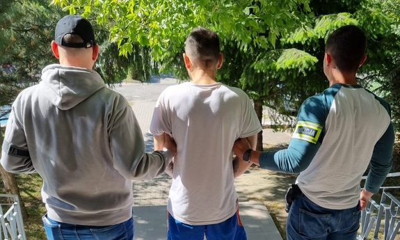 dwaj funkcjonariusze z zatrzymanym mężczyzną stoją na schodach
