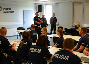 zebrani policjanci siedzą za stołami, przemawia do nich oficer