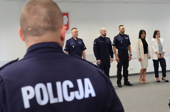 widok na plecy Policjanta w koszulce z napisem Policja i stojący przed nim oficerowie