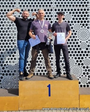 trzej mężczyźni na podium stoją na stopniu dla zwycięzców I miejsca