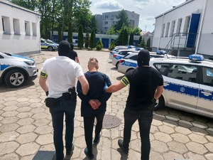 na zdjęciu dwóch policjantów prowadzi zatrzymanego mężczyznę