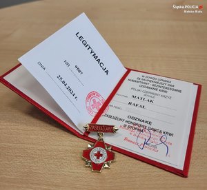 leżąca na stole, otwarta legitymacja zasłużonego honorowego dawcy krwi i odznaczenie