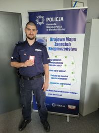 umundurowany policjant z trzymaną w dłoni legitymacją zasłużonego honorowego dawcy krwi pozuje do zdjęcia
