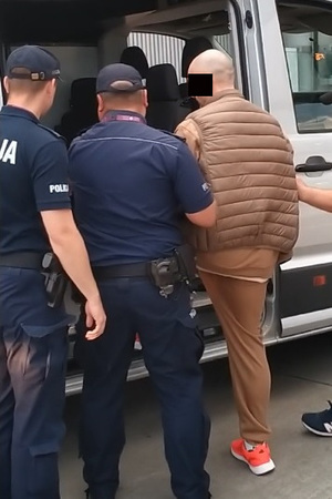 Policjanci wprowadzają konwojowanego mężczyznę do radiowozu
