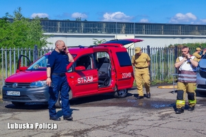 Policjant wraz ze strażakami obok pojazdów służbowych