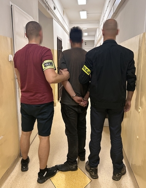 dwaj nieumundurowani policjanci trzymają zatrzymanego mężczyznę zakutego w kajdanki