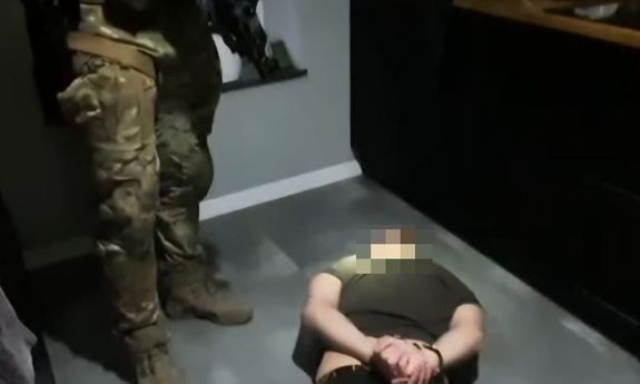 zatrzymany mężczyzna leży na podłodze. Nad nim stoją policjanci