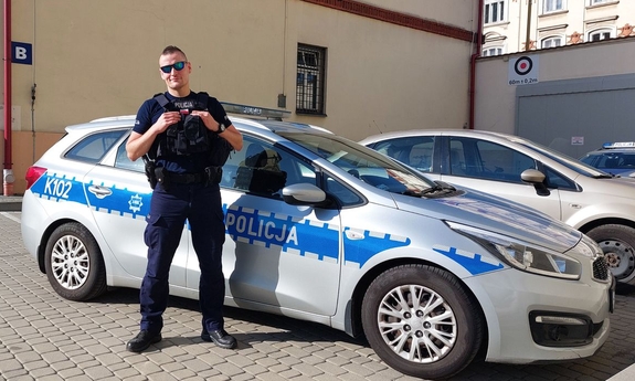 w mundurze, na tle policyjnego radiowozu stoi st. post. Tomasz Pipała