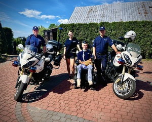 dwaj policjanci na motocyklach, pomiędzy nimi Wojtek na wózku, obok niego opiekunka